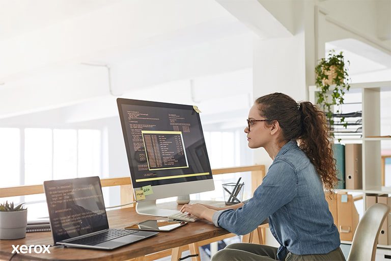 A woman at her desk, engaged with a computer and laptop, demonstrating productivity in a modern workspace. A woman at her desk, engaged with a computer and laptop, demonstrating productivity in a modern workspace.