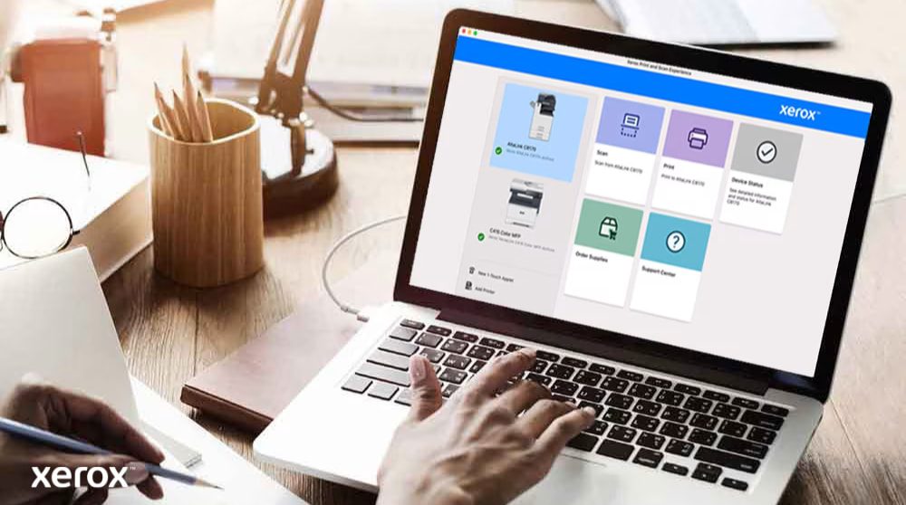 A person's hands are on a laptop keyboard, and the screen displays the Xerox Print and Scan Experience interface with options like Scan, Print, Device Status, Order Supplies, and Support Center, indicating user-friendly control.