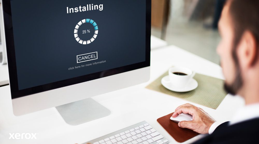 A close-up view of a computer monitor displaying an "Installing" progress bar at 25%, with a person's hand on a computer mouse next to a coffee cup, illustrating easy software setup.